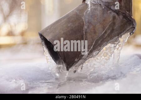 Drainpipe an der Ecke des Hauses mit Eis und Eiszapfen bedeckt Stockfoto