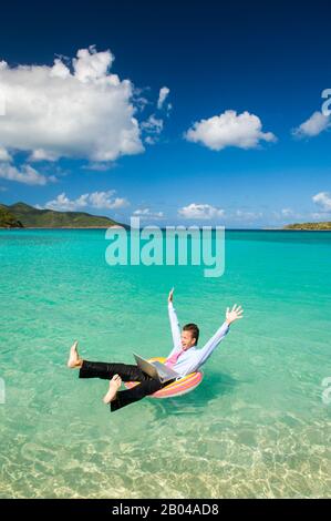 Aufgeregter Büroangestellter, der seine Arme und Beine in einer Feier hochwarf, die mit seinem Laptop im Freien in einem tropischen Inselmeer schwebte Stockfoto