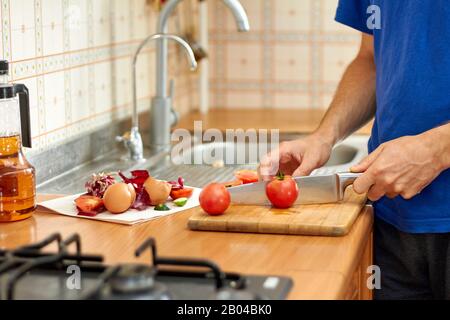 Ein Mann schneidet Tomaten. Lebensmittelabfälle und -Reste bei der Zubereitung von Speisen in der Küche. Nahaufnahme, selektiver Fokus Stockfoto