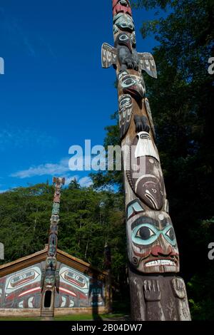 Tlingit Totempfahl mit Clanhaus im Hintergrund im Totem Bight State Historical Park in Ketchikan, Südost-Alaska, USA. Stockfoto