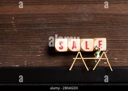 Kleine Malerfigur und Würfel mit dem Wort "Sale" auf Holzhintergrund Stockfoto