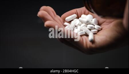 Halten Sie medizinische Pillen und Tabletten und lassen Sie sie auf schwarzem Hintergrund fallen Stockfoto