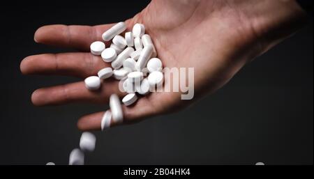 Halten Sie medizinische Pillen und Tabletten und lassen Sie sie auf schwarzem Hintergrund fallen Stockfoto