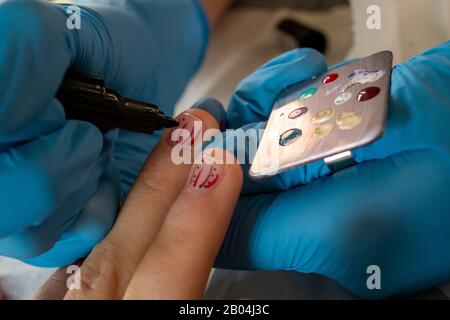 Nahaufnahme des Nagelkünstlers mit Punkten für das Design auf kurzen Fingernägeln junger Frau. Stockfoto