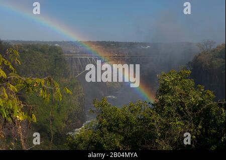 Blick von Sambia auf die Victoria Falls Bridge zwischen Sambia und Simbabwe mit Regenbogen im Sprühbild der Stürze. Stockfoto