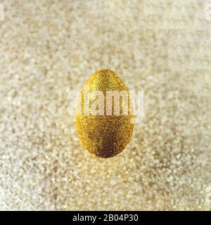 In der Luft hängt ein goldenes Ei. Auf einem strukturierten goldenen Hintergrund. Das Konzept zum Thema Ostern. Stockfoto