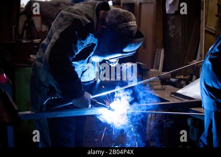 Unanstiraler Arbeiter in Maske, beim Schweißen von Metall mit hellem Licht, Rauch und Funken Stockfoto