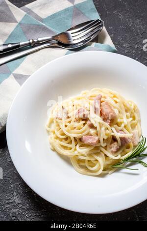 Nudelkarbonara wird auf einer tiefen Platte serviert, die mit Rosmarin verziert ist. Abendessen. Stockfoto