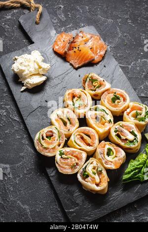 Pfannkuchenrollen mit geräuchertem Lachs und Frischkäse auf schwarzem Steingrund Stockfoto