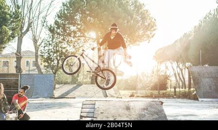 Eine Gruppe von Freunden, die einen Biker beim Freestyle-Sprung mit dem bmx-Fahrrad beobachten - Junge Leute haben Spaß mit extremer Sporterholung in der städtischen Par Stockfoto