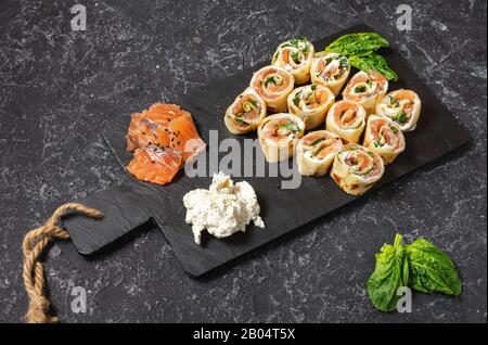 Pfannkuchenrollen mit geräuchertem Lachs und Frischkäse auf schwarzem Steingrund Stockfoto