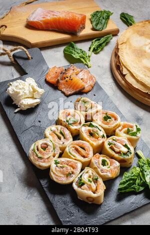 Pfannkuchenrollen mit Räucherlachs und Frischkäse auf Betongrund. Stockfoto