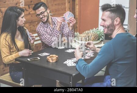 Eine Gruppe von Freunden, die Karten spielen, die an einem Tisch in den Ferien sitzen, Camping Haus - Junge glückliche Leute, die Spaß haben, zusammen zu lachen - Soft Focus Stockfoto