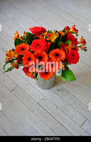 Farbenfrohes orangefarbenes und rotes Blumenarrangement mit Freesia-Blumen, Gerbera-Gänseblümchen und Rosen Stockfoto