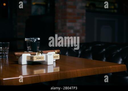 Rauchende Zigarre in einem Aschenbecher und gläserner Cognac auf dunklem Hintergrund Stockfoto