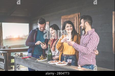 Fröhliche junge Paare, die Rotwein toben und im Holzhaus im Hinterhof grillen - Fröhliche Leute, die im Sommer bei Sonnenuntergang Spaß haben - Konzentrieren Sich auf RI Stockfoto