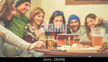 Fröhliche Freunde, die Biere toben und Videos auf dem Tablet im Chalet Pub in den Bergen ansehen - Junge Leute, die im Winterurlaub Spaß haben - Freundschaft versunken Stockfoto