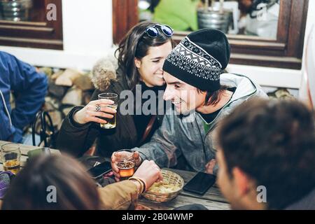 Fröhliche reiche Freunde, die am Abend im Chalet-Pub-Restaurant in den Bergen Bier toben - Junge Leute, die im Winterurlaub Spaß haben - Friendship Konz Stockfoto