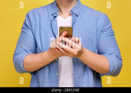Ein Mann in einem blauen Hemd auf gelbem Hintergrund hält ein Smartphone. Konzept der Online-Bestellung von Waren. Nahaufnahme. Stockfoto