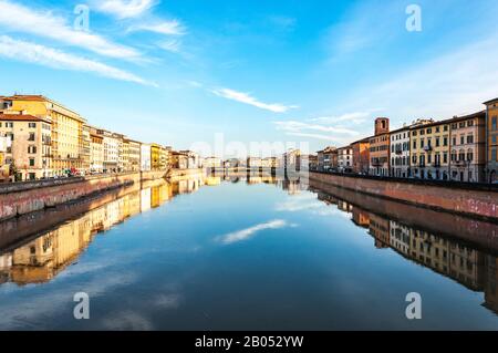 Spektakulärer Blick auf den Fluss in Pisa zusammen mit farbigen Häusern, die sich in Wasser und blauem Himmel mit kleinen weißen Wolken widerspiegeln Stockfoto