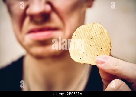 Ein Mann sitzt mit Spänen in der Hand und er ist angeekelt davon. Nahaufnahme. Stockfoto