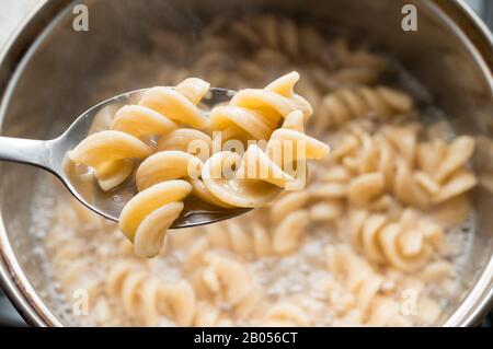 Ein Löffel mit Vollkornfusilli auf Nudelgrund, in einem Topf gekocht. Gesunde Ernährung. Stockfoto