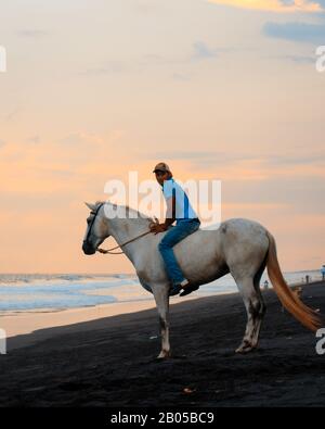 Mann zu Pferd am Strand bei Sonnenuntergang Stockfoto