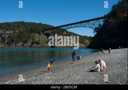 Menschen am North Beach des Deception Pass State Park auf der Insel Whidbey Island, Washington State, Vereinigte Staaten mit Deception Pass Bridge im Hintergrund Stockfoto