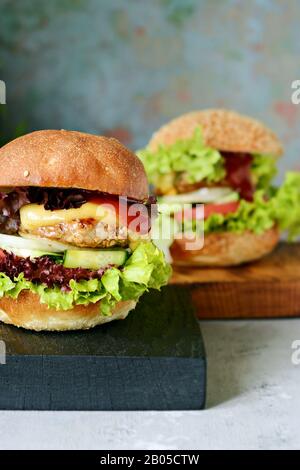 Frische, leckere Burger mit saftiger Häutung, grünem Salat, Käse und Gemüse auf einem Schneidebrett. Hausgemachter Hamburger. Stockfoto