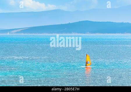 Windsurfer auf gelbem Segelbrett in der Adria in Bol auf der Insel Brac bei Split, Kroatien. Wassersport Windsurfen im türkisfarbenen Wasser und in den Bergen Stockfoto