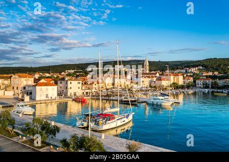 Supetar auf der Insel Brac in der Nähe von Split, Kroatien. Kleine Küstenstadt mit Promenade und Hafen mit weißen Booten, Palmen, Cafés, Häusern und Kirche. Touri Stockfoto