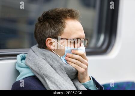 Nahaufnahme des kranken Mannes in Brillen, die in Schal gewickelt waren, sich krank fühlend, hustend, Schutzmaske gegen übertragbare Infektionskrankheiten tragend, Kovid-19 Stockfoto