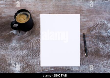 Leeres Papierblatt mit schwarzem Kaffeebecher und Stift auf dem rustikalen Holztisch Stockfoto