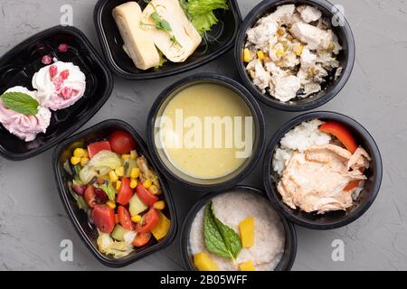 Gesunde Business-Lunch-Container am Arbeitsplatz. Sahnesuppe mit Wachteleiern, Gemüse und gebratenem Hühnerlöffel auf grauem Tisch, Draufsicht Stockfoto