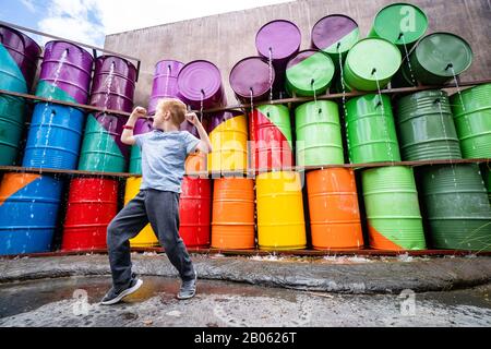 Jungen Jungen, Der Muskeln in der städtischen Gasse mit Regenbogen aus Farbigen Fässern und Wasser Beugt Stockfoto