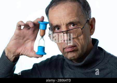 Die Zeit ist flüchtig. Konzept des Alterns und des Älterwerdens. Sanduhr in den Händen eines älteren Mannes auf weißem Hintergrund. Stockfoto