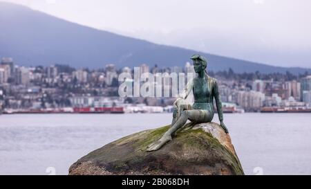 Vancouver, BC Canada - 14. März 2019: Eine Statue eines Mädchens in einem Badeanzug auf einem Felsbrocken an einem Ufer des Vancouver Harbour mit Blick auf die Stadt im Hintergrund Stockfoto