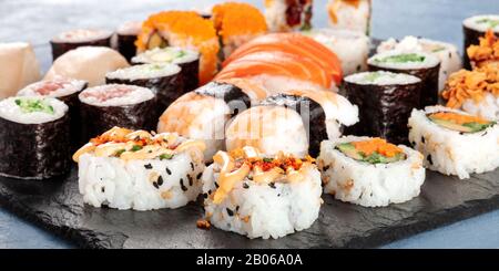 Großes Sushi in Panorama-Nahaufnahme. Eine Auswahl an verschiedenen Maki, Nigiri und Brötchen Stockfoto