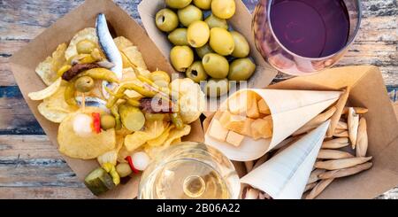 Tapas und Pinchos, Panorama-Blick über die Decke. Käse, Jamon und Oliven, gildas und Kartoffelchips, mit Brille aus Rot- und Weißwein, auf einem Holztisch Stockfoto
