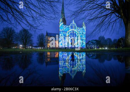 Die Menschen sehen, wie Lichtprojektionen die Westfront der Kathedrale von Salisbury bedecken, wo eine Licht- und Tonkunst-Installation mit dem Titel Sarum Lights das 800-jährige Jubiläum der Kathedrale im Jahr 2020 markiert, indem sie die Innen- und Außenbeleuchtung zusammen mit Musik beleuchten. Stockfoto