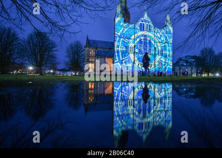 Die Menschen sehen, wie Lichtprojektionen die Westfront der Kathedrale von Salisbury bedecken, wo eine Licht- und Tonkunst-Installation mit dem Titel Sarum Lights das 800-jährige Jubiläum der Kathedrale im Jahr 2020 markiert, indem sie die Innen- und Außenbeleuchtung zusammen mit Musik beleuchten. Stockfoto