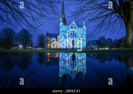 Die Menschen sehen, wie Lichtprojektionen die Westfront der Kathedrale von Salisbury bedecken, wo eine Licht- und Tonkunst-Installation mit dem Titel Sarum Lights das 800-jährige Jubiläum der Kathedrale im Jahr 2020 markiert, indem sie die Innen- und Außenbeleuchtung zusammen mit Musik beleuchten. Stockfoto