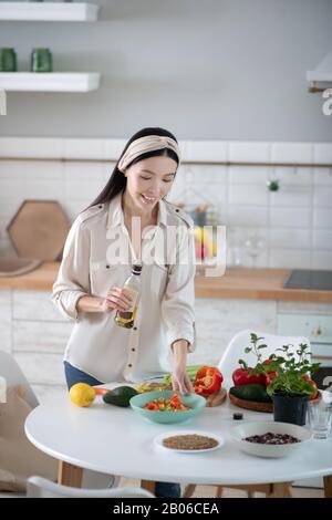 Schöne junge Frau mit Olivenöl, die auf einen Salat blickt. Stockfoto