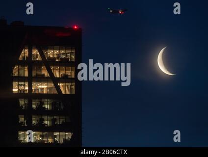 London, Großbritannien. Feb. 2020. Der schwingende Mond ist am Morgen neben einem Büroturm zu sehen, während ein Flugzeug darüber fliegt. Kredit: Robert Michael / dpa-Zentralbild / dpa / Alamy Live News Stockfoto
