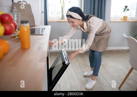 Junge Frau in einer Schürze, die sich zum Ofen neigt. Stockfoto