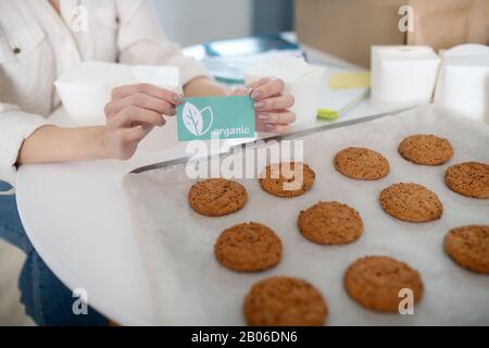 Weibliche Hände, die eine Karte in der Nähe eines Tabletts mit hausgemachten Kuchen halten. Stockfoto