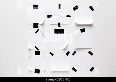 Weißes geripptes Notizpapier, das mit schwarzem Klebeband auf weißem Hintergrund haftet. Stockfoto