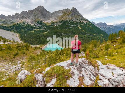 Junge Frau, Wanderer steht auf Felsen und blickt auf den türkisgrünen Sorapisser See und die Berglandschaft, die Dolmen, Belluno, Italien Stockfoto