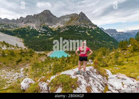 Junge Frau, Wanderer steht auf Felsen und blickt auf den türkisgrünen Sorapisser See und die Berglandschaft, die Dolmen, Belluno, Italien Stockfoto