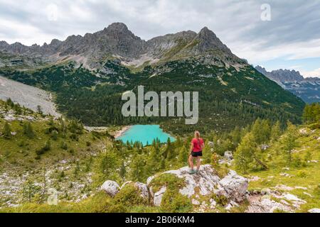 Junge Frau, Wanderer steht auf Felsen und blickt auf den türkisgrünen Sorapisser See und die Berglandschaft, die Dolmen, Belluno, Italien Stockfoto